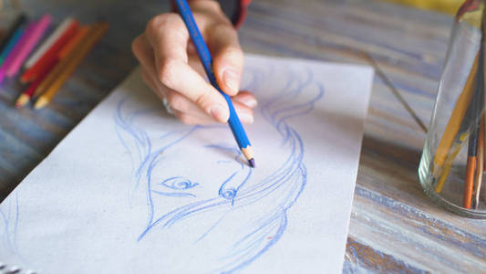 用铅笔在纸笔记本上画女性手绘剪影特写。妇女艺术家在工作