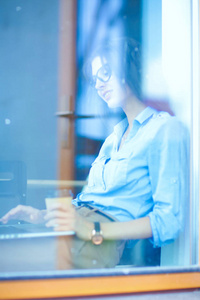 年轻女子坐在办公室桌的笔记本电脑，通过窗口视图。年轻的女人