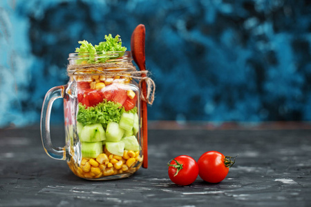在玻璃罐子里放蔬菜沙拉。汤匙和樱桃西红柿