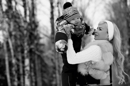 一个年轻的母亲走在一个冬天的一天, 怀里抱着一个孩子。