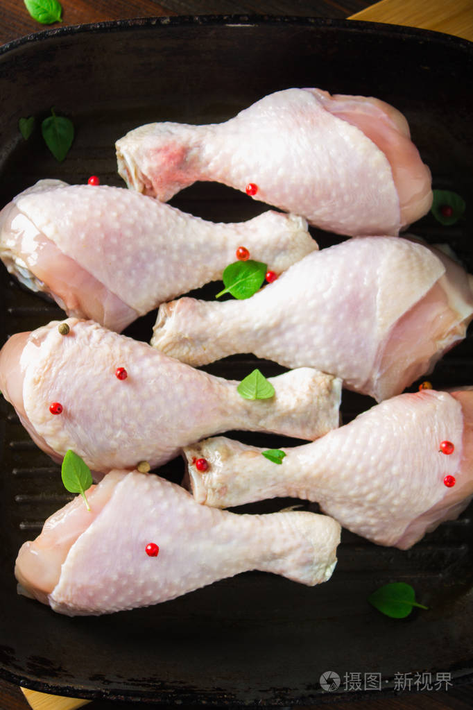 生鸡腿在一个木桌上的煎锅里烹调用的肉类配料顶部视图