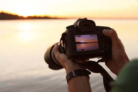 男子摄影师持有专业相机与照片的河畔日落显示