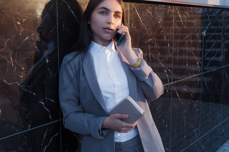 年轻迷人的女孩在商务西装使用电话。生活方式和商业肖像