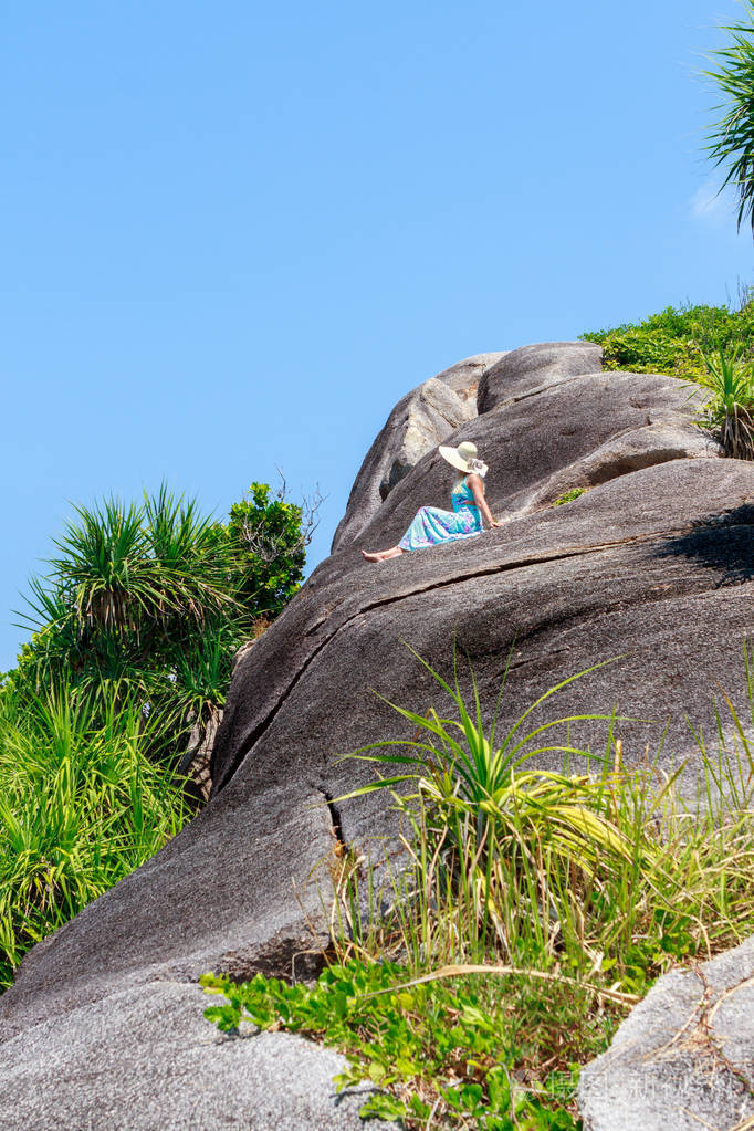 穿着蓝色连衣裙的女孩坐在石头上, 看着地平线的距离