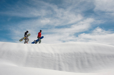 两个年轻的滑雪走上山与滑雪板在他们手中的背景晴朗的蓝天