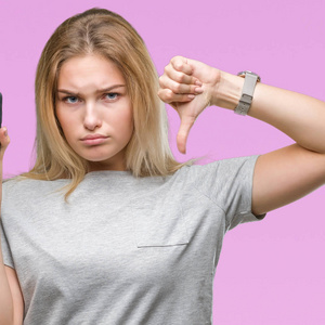 年轻的白种人妇女显示屏幕的智能手机在孤立的背景与愤怒的脸, 否定的符号显示不喜欢拇指向下, 拒绝概念