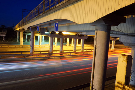 空沥青路下桥在夜间与红灯小径背景。夜间城市场景与车光小径在隧道。长时间曝光