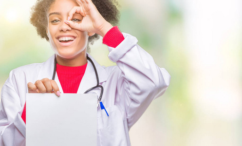 年轻的美国黑人医生妇女持有空白纸在孤立的背景与愉快的脸微笑做 ok 标志与手在眼睛看通过手指