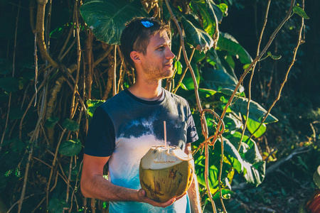 站在丛林里的年轻人手里拿着一杯新鲜的椰子饮料