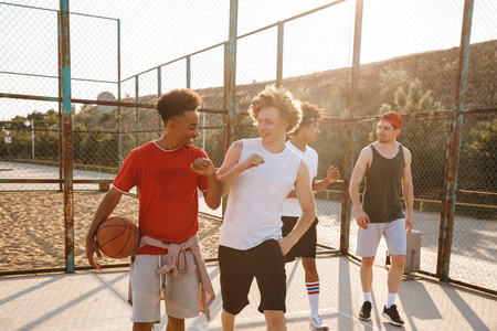 在夏日阳光明媚的日子里, 快乐的年轻人的肖像篮球运动员沿着操场散步