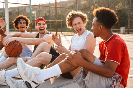 一群年轻欢快的多民族男子篮球运动员休息在运动场上, 谈论