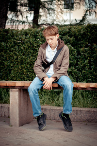 坐在公园长凳上的可悲少年