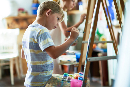 艺术课上画架上的可爱男孩绘画的侧面视图肖像, 专心于他的杰作