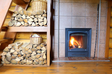 木炉子和木柴在农村的木屋里。房间内部的一部分, 在农村的房子, 一堆木柴和一个燃烧的木材炉子