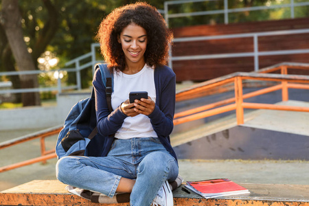 快乐非洲青年妇女的形象坐在户外公园使用手机