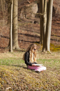 金发女孩坐在草读一本书。户外公园