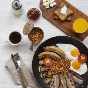 全英式早餐在平底锅与煎蛋熏肉豆类香肠和敬酒在白色木桌, 顶上的看法。特写
