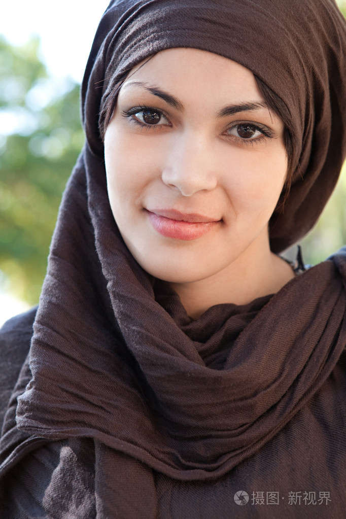 穆斯林的年轻女人头围围巾和相机在微笑