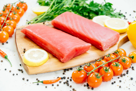用蔬菜和烹调配料的木制砧板上的生金枪鱼鱼片肉