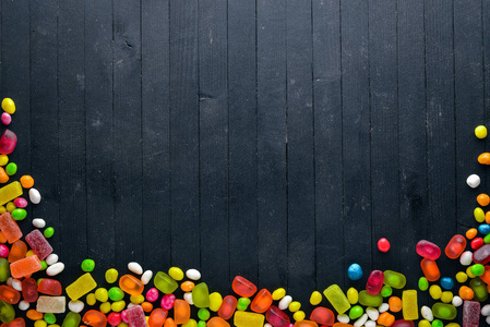 彩色糖果, 糖果和棒糖。在一个黑色的木制背景。顶部视图。自由空间