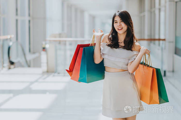 愉快的亚洲美丽的妇女享受和微笑与五颜六色的购物袋在她的两只手在