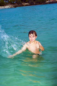 英俊的男孩在海洋中有乐趣和显示拇指