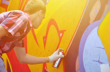 一位年轻的红头发涂鸦艺术家在墙上画了一幅新的涂鸦。在墙特写画涂鸦的过程的照片。街头艺术的概念与非法破坏