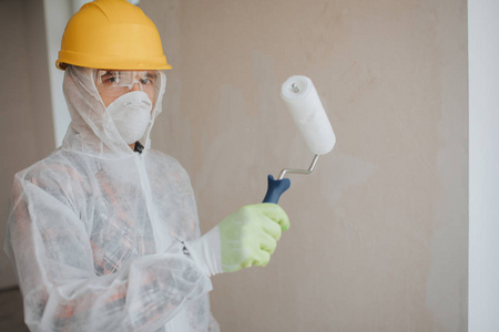 带油漆辊的工人.他穿着防护服戴着面具照片