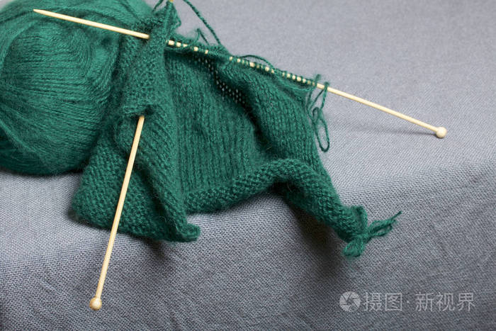 针织木制针织.一根深绿色的线球和木制针织针在未完成的针织