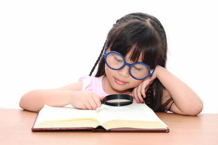 亚洲小女孩读一本书用放大镜