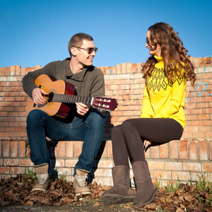 浪漫的年轻夫妇肖像在蓝蓝的天空下弹吉他