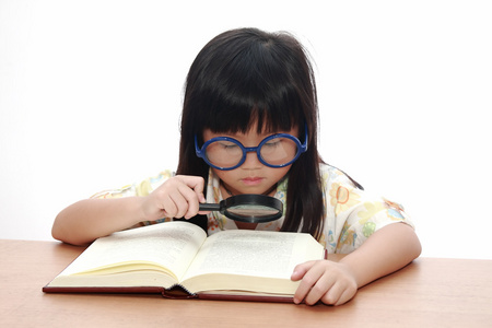 亚洲小女孩与孤立的放大镜读一本书