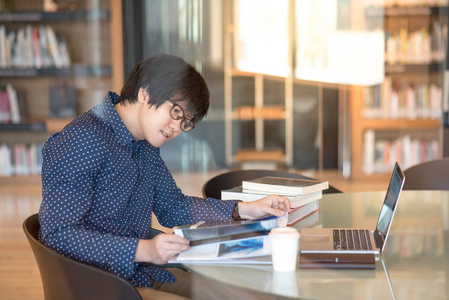 图书馆里的亚洲年轻男子大学学生阅读本书