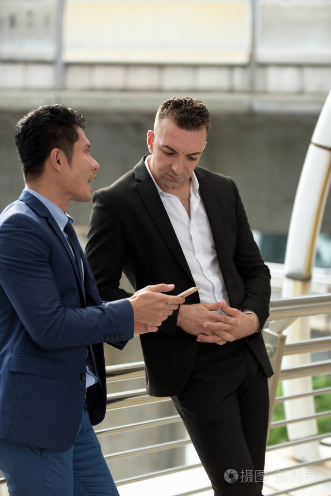 两个生意人在户外聊天.两个年轻的商界人士站在商业区中间