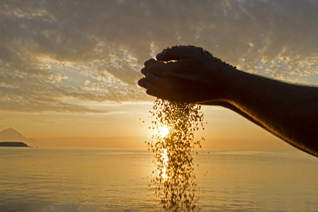 行业时钟手打谷生命时间流逝的概念.人手在日出背景上倒沙照片