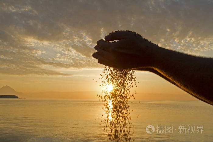 生命时间流逝的概念人手在日出背景上倒沙