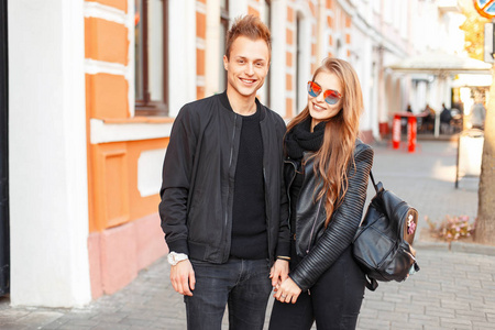 时尚美丽的情侣在太阳镜和花哨的黑色衣服与一个袋子在街上