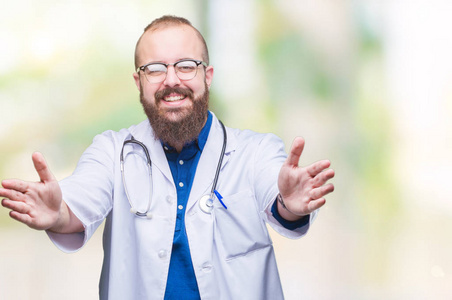 年轻的高加索医生男子穿着医疗白色外套在孤立的背景看着镜头微笑着张开双臂拥抱。拥抱幸福的快乐表情