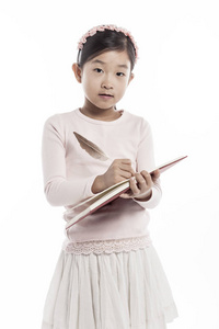 小女孩拿着一本书与羽毛平底锅, 当站立在演播室时, 隔绝在白色背景