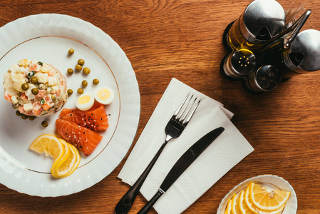 俄罗斯沙拉盘子上有散落的豌豆煮鸡蛋和鱼片, 桌子上有刀叉和餐巾