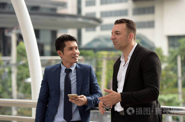 两个生意人在户外聊天.两个年轻的商界人士站在商业区中间