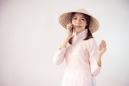 美丽的女人在粉红色的礼服和越南帽子持有智能手机