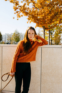 美丽可爱的 redhaired 女孩在一个时髦的橙色毛衣在一个秋季公园的轻栅栏摆姿势