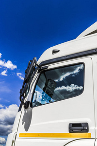 蓝天上的白色积云反映在一辆大型卡车的侧面窗户和后视镜上。