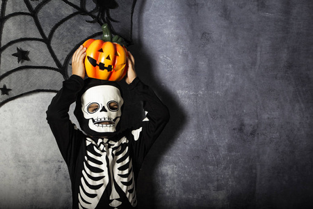 小男孩在骷髅服装举行万圣节南瓜照片