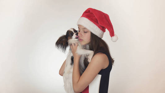 美丽的少女在一个圣诞老人帽子和狗大陆玩具猎犬比快乐亲吻和鬼混在白色背景
