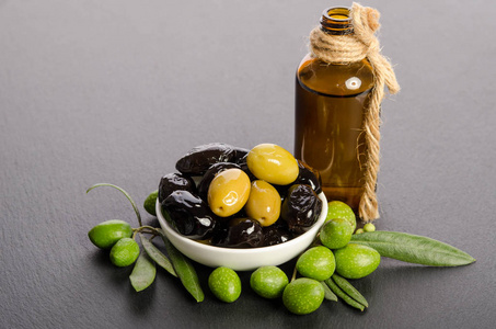 黑色和绿色的橄榄混合中的初榨橄榄油和瓷器碗
