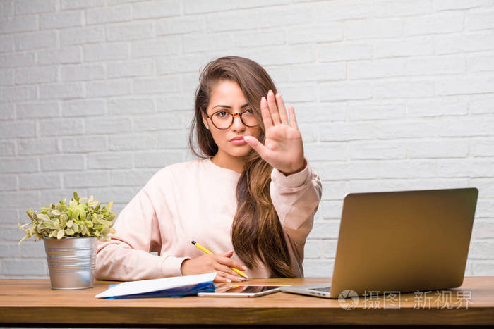 年轻的学生拉丁妇女的肖像坐在办公桌上认真和确定