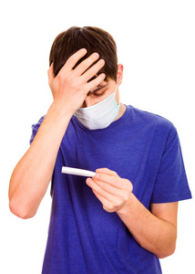 在流感面具的年轻人检查在白色背景查出的温度计