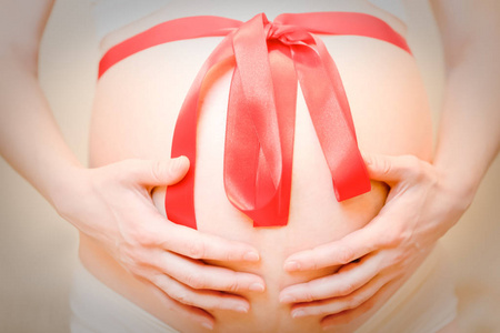 孕妇穿着白色内衣, 手捧腹部和红色 猩红 缎带在腹部。怀孕的少妇